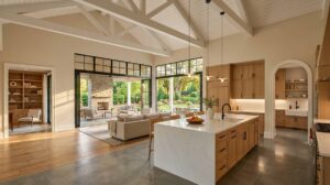 Blog | Cooper Development Group Open-concept luxury custom home interior in Charlotte, NC with white oak cabinetry, scullery pantry visible through arched doorway, vaulted ceiling with exposed beams, indoor-outdoor connection to a covered outdoor living room with stone fireplace